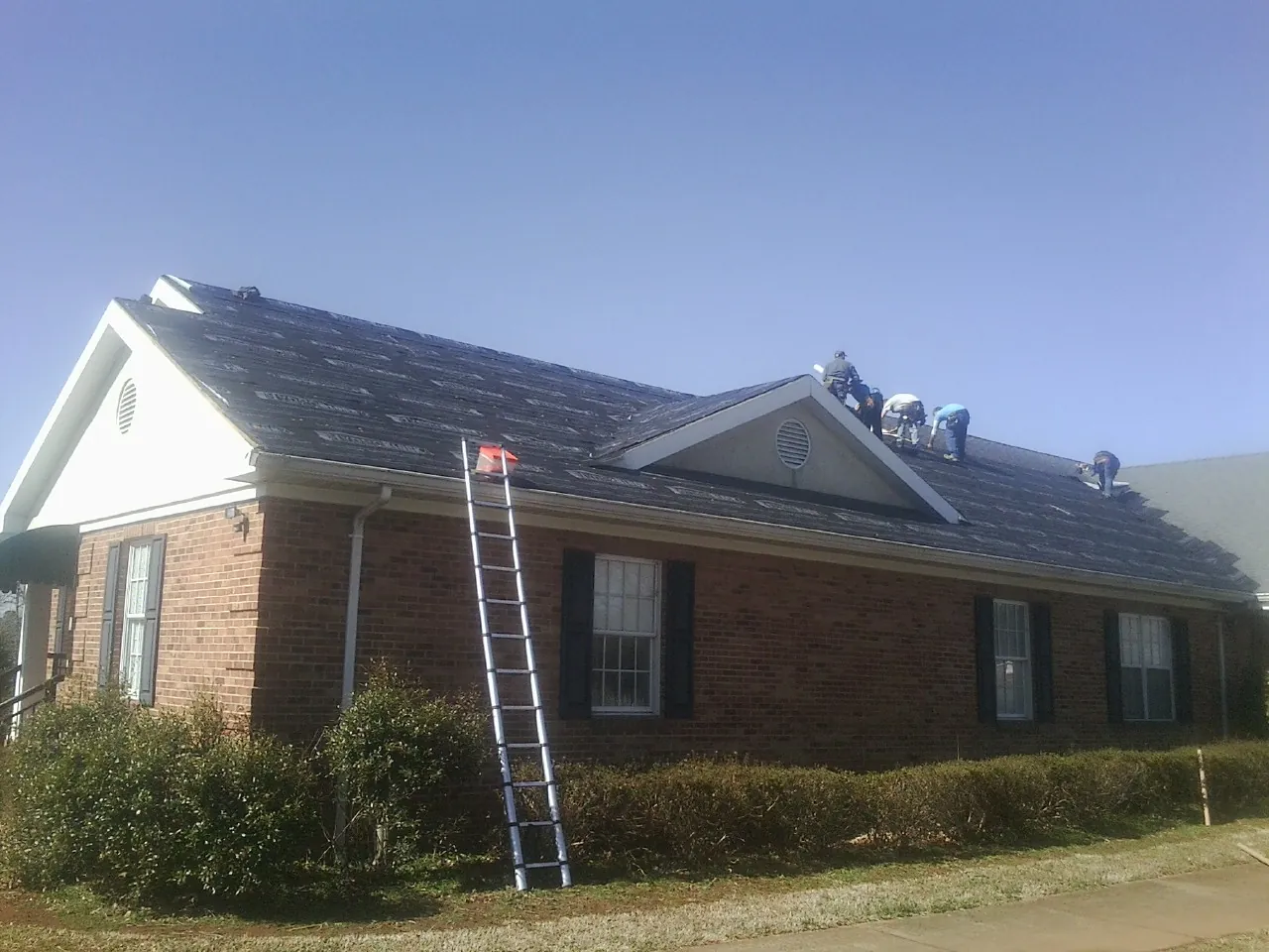 Crew tearing shingles off a brick ranch roof with a ladder set — Metal Roof Repair work by our crew in New Bedford