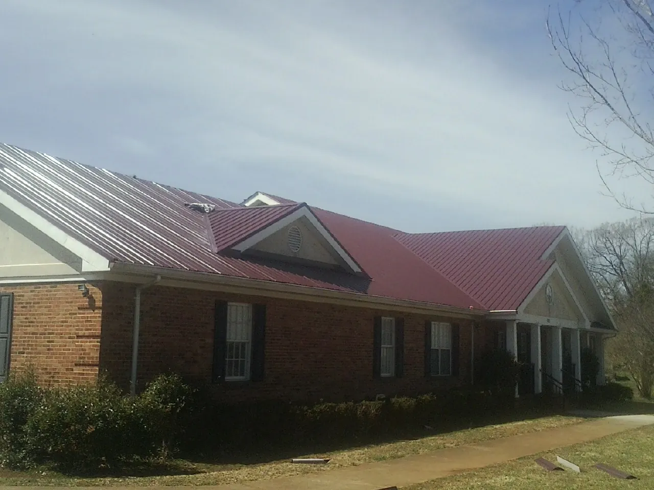Red metal roof with gabled entries on a long brick building, from a Hail Damage Roof Repair job in New Bedford
